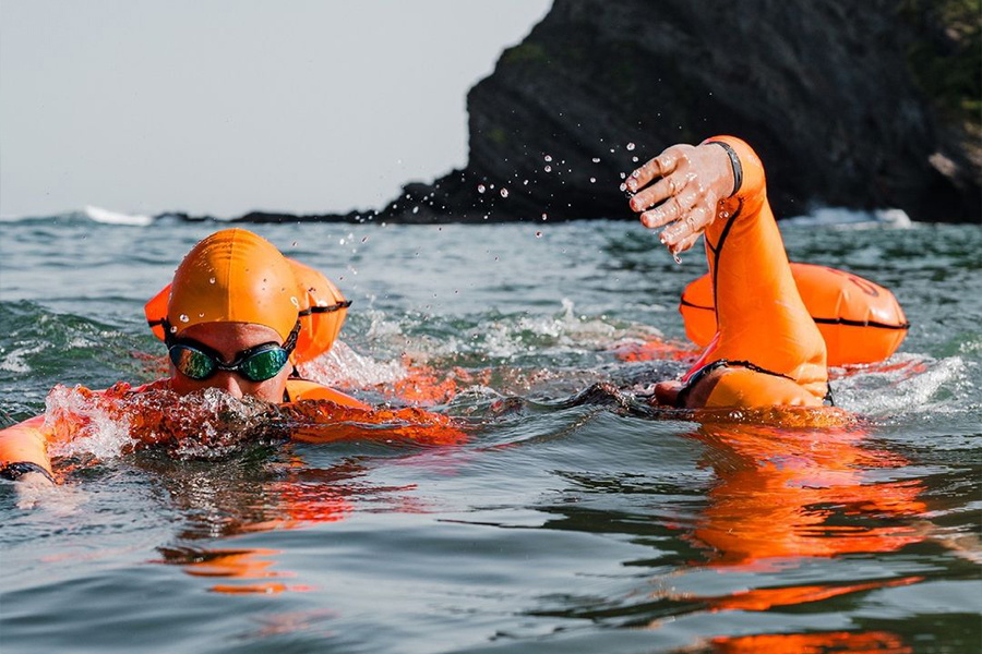 Open water swimmer in an orange cap and goggles swimming beside an inflated orange tow float
