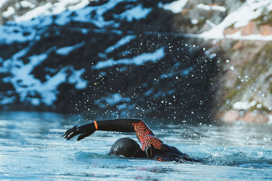 Open water swimmer front crawling in a black wetsuit with orange sleeve panels beside cliffs