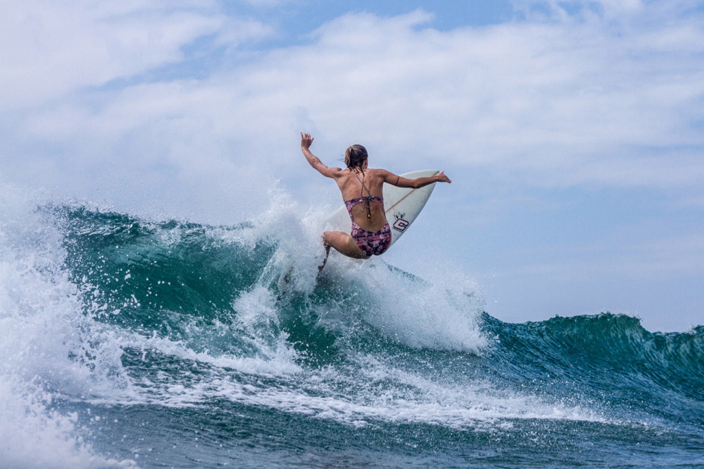 Surfer in a bikini snapping off the lip of a breaking wave, spray flying behind the board