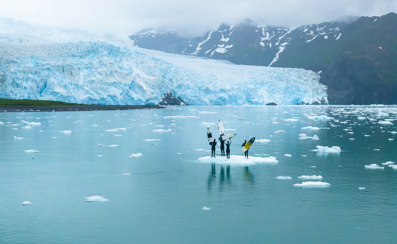 Group of stand-up paddleboarders on icy water in front of a vast blue glacier